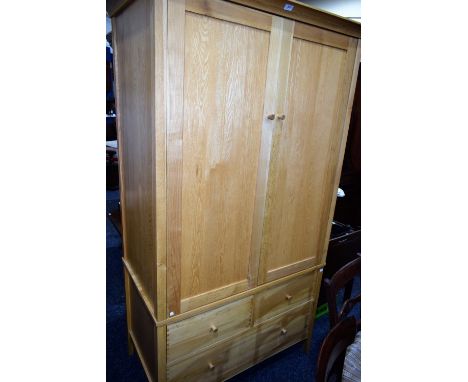 A contemporary oak wardrobe, concave cornice above two panel doors enclosing a hanging rail, the base with two short over one