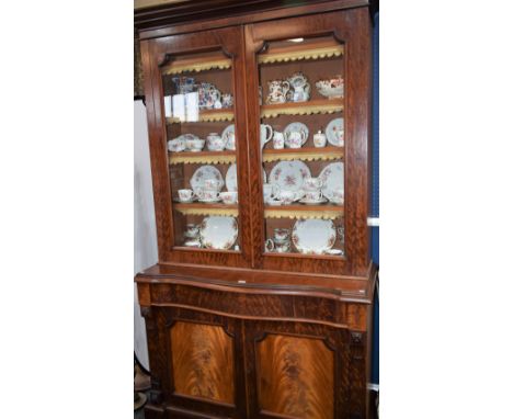 A Victorian mahogany library bookcase, outswept cornice above a pair of glazed doors enclosing four shelves, the projecting b