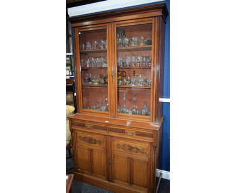 An Arts and Crafts library bookcase, dentil cornice above a pair of glazed doors enclosing shelves, the projecting base with 