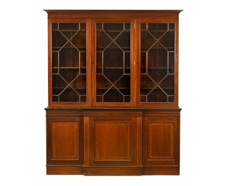 An Edwardian inlaid mahogany breakfront bookcase, the top with dentil cornice and with three astragal glazed doors, containin