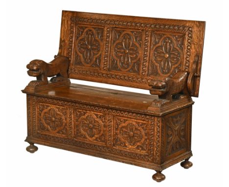 An early 20th century oak carved monks bench, with three panelled top, the base with carved lions lift up seat and further th