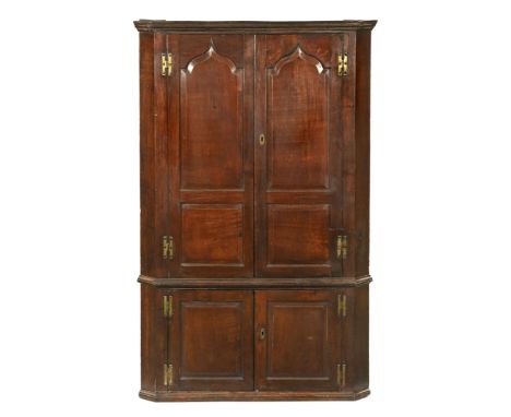A Georgian oak double corner cupboard, the upper section with arched panelled doors and opening to a blue painted interior wi
