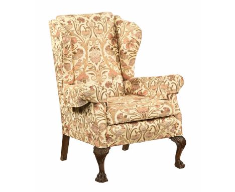An Edwardian wing armchair, upholstered in floral and bird patterned material raised on carved front legs with hairy paw feet