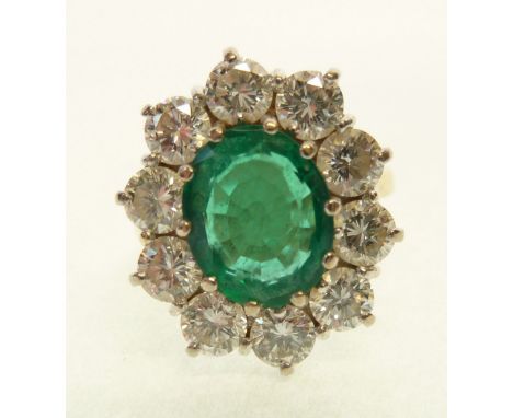 18CT GOLD EMERALD AND DIAMOND CLUSTER RING, claw set with an oval cut emerald (probably synthetic), with a cluster surround o