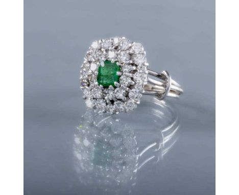 AN EMERALD AND DIAMOND CLUSTER COCKTAIL RING, the central oval facet cut emerald claw set to a double border of brilliant cut