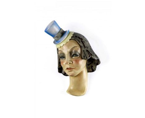 AN ART DECO LENCI POTTERY WALL MASK, the stylised heavy lidded face wearing a small blue and primrose yellow top hat on her g