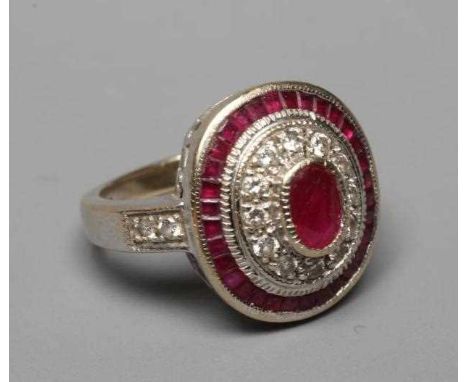 A RUBY AND DIAMOND TARGET PLAQUE RING, the oval cut ruby of approximately 1ct collet set to a border of point set small brill