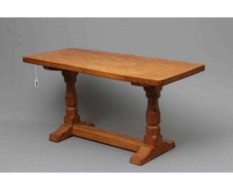 A ROBERT THOMPSON ADZED OAK COFFEE TABLE, the oblong top raised on trestle base with turned faceted supports and square sledg