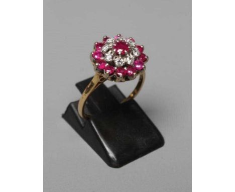 A RUBY AND DIAMOND CLUSTER RING, the central ruby claw set to a border of eight small diamonds and a further border of twelve