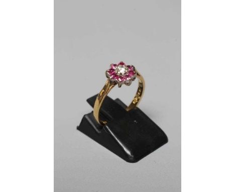 A CLUSTER RING, the central round brilliant cut diamond of approximately 0.60cts to a border of eight small facet cut ruby co