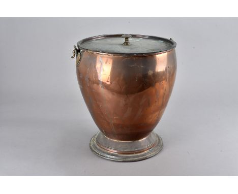 An Edwardian copper coal scuttle, of circular tapered form with swing handle and lift off lid supported on a circular spreadi