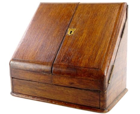 An Edwardian oak slope top stationery cabinet, the hinged lid enclosing a fitted interior with an inkwell, 30cm wide.