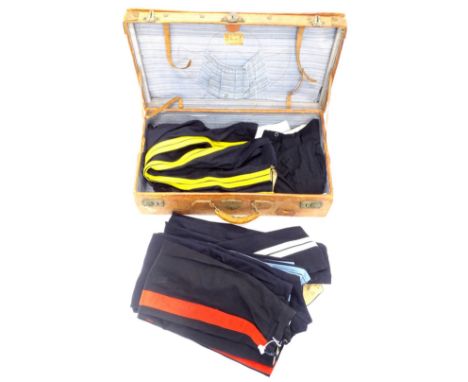 A vintage leather suitcase, containing various pairs of military trousers, mainly with side piping and a pair of leather chap