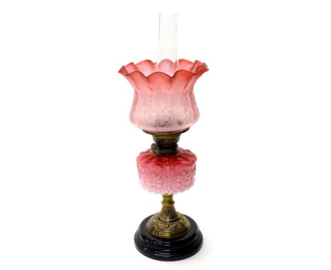 A Victorian cast brass oil lamp, with two tone pink reservoir, and a cranberry tinted etched shade decorated with flowers and