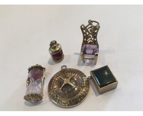 A collection of 9ct gold charms in the form of a roulette wheel chair, an hour glass a ships lamp and a box set with a polish