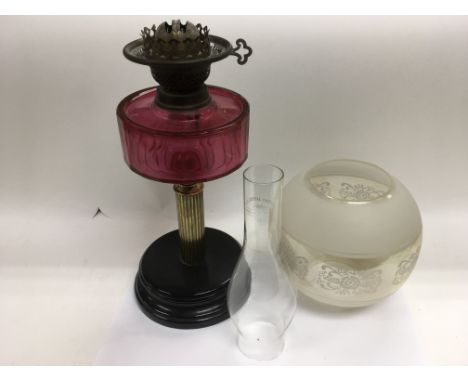 An oil lamp with a cranberry glass reservoir.