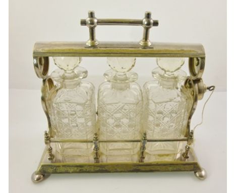 A LATE VICTORIAN SILVER PLATED THREE DECANTER TANTALUS, with chased decoration, raised on bun feet, containing three square c