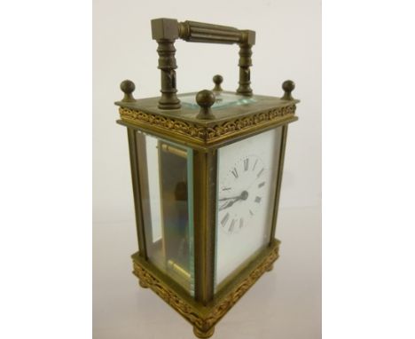 A FOUR GLASS BRASS FRAMED CARRIAGE CLOCK with decorative cast floral frieze panel to the base, white enamel dial with Roman n