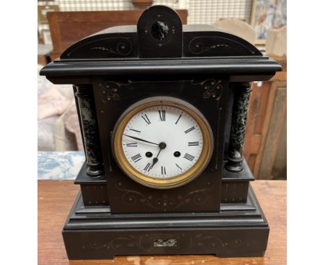 A black slate mantle clock, with a shaped top and columns, the circular enamel dial with Roman numerals