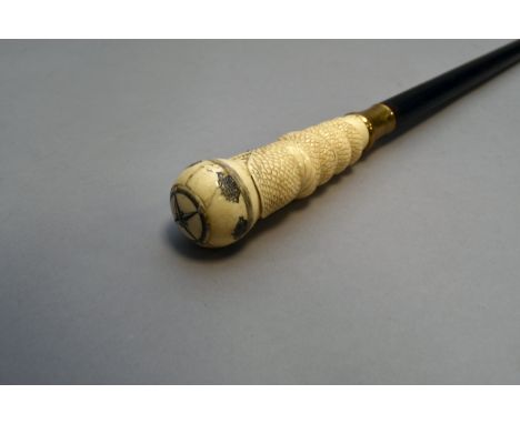 A carved bone-handled ebonised cane of nautical interest, the head carved as a curled scaly serpent holding a ball pommel in 