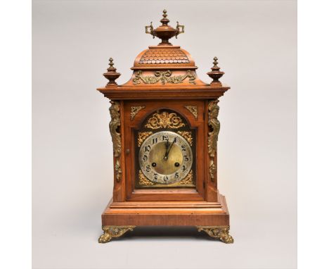 A late 19th century German bracket clock, of architectural form with a covered urn finial above a shaped 'tiled' roof, over a