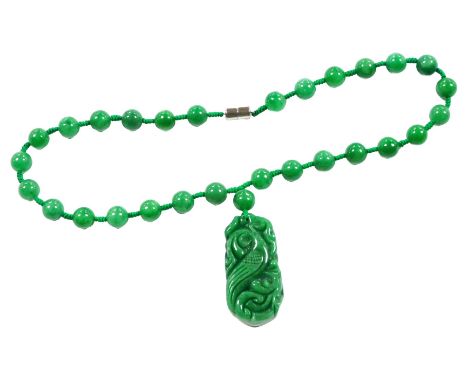 A green jade necklace, with a pendant carved with a bird and scrolling leaves, and twenty nine beads, on a magnetic clasp. 
