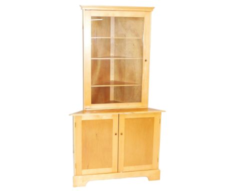 A beech and teak corner cabinet, with an outswept pediment over a glazed door enclosing three triangular shelves, above a pai