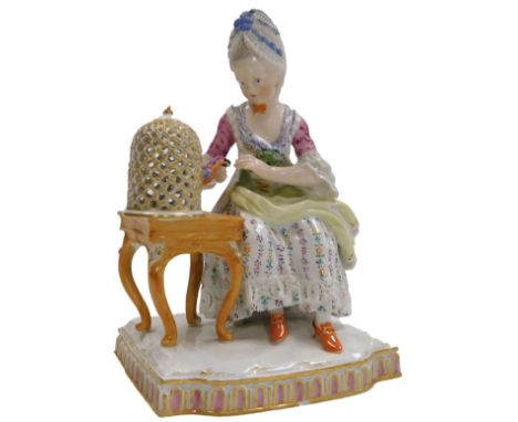 A late 19thC Meissen porcelain figure, of a lady seated at a table with a birdcage, blue cross swords mark, 16cm high.