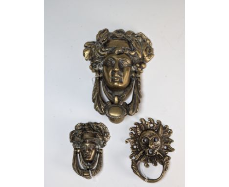 A large Georgian brass Door Knocker, in the form of a classical female mask, H 18 cm, together with two more 19th century bra