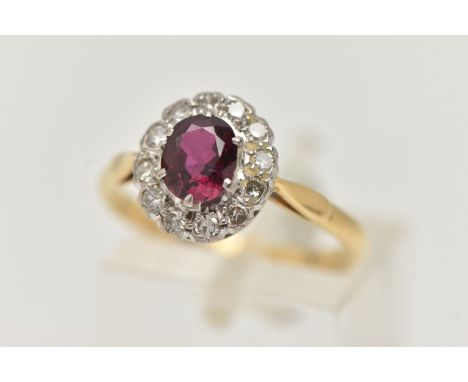A RUBY AND DIAMOND CLUSTER RING, a principally set oval cut ruby, prong set in white metal, with a surround of twelve single 
