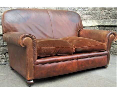 An early 20th century two seat sofa with rolled arms, tan faux leather upholstered finish with loose upholstered cushions and