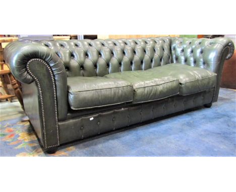 A traditional three seat Chesterfield sofa with buttoned dark green faux leather upholstered finish, loose seat cushions and 