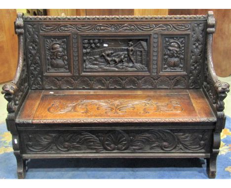 A 19th century carved oak hall box settle with lions mask arms, portrait and landscape panels and repeating foliate detail ov