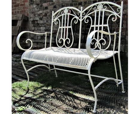 A contemporary cream painted light steel framed two seat garden bench with scrolled lyre shaped twin panelled back over a cur