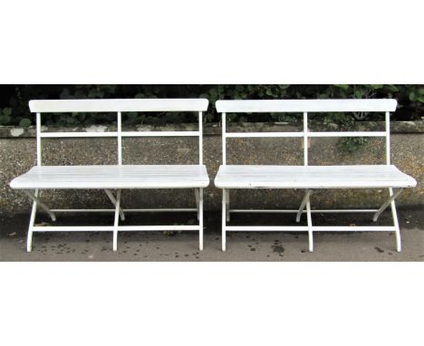 A pair of cream painted light steel framed two seat benches with timber lathes and rail back raised on folding X framed suppo