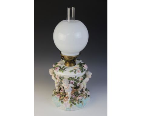 An German florally encrusted porcelain oil lamp, 19th century, modelled with four putti supporting the reservoir, the base wi