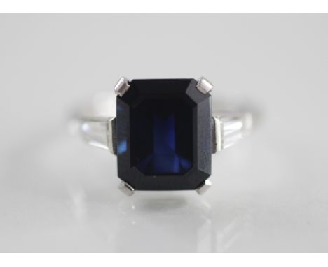 An Art Deco sapphire and diamond ring, the central rectangular step cut (untested) sapphire measuring 11mm x 8mm, claw set in