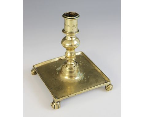 An early square form brass candlestick, possibly Dutch 17th century, the baluster knopped stem upon a square drip tray raised