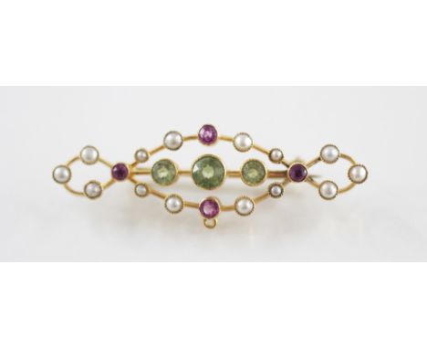 An early 20th century peridot, ruby and pearl set bar brooch, comprising three mixed cut peridots, set to a scrolling border 