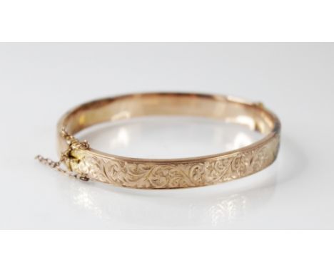 An early 20th century 9ct gold hinged bangle, with engraved scrolling decoration to front, 8mm wide, tongue and box snap clas