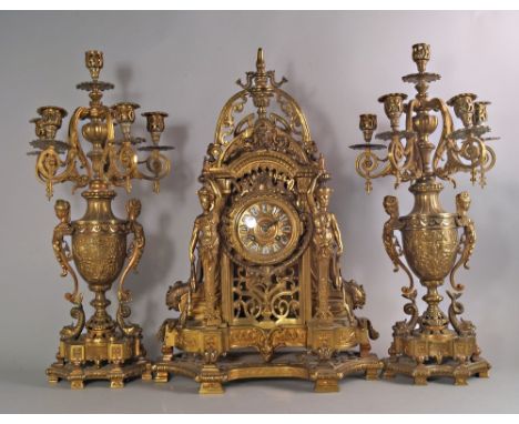 A French gilt metal clock garniture, late 19th/early 20th century, the clock of pierced architectural form, moulded with grot