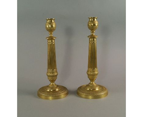 A pair of gilt bronze candlesticks, 19th century, with urn shaped nozzles above tapering flute columns, with spreading steppe