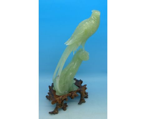 A carved jade model of a bird of paradise on a carved wooden stand, beak a/f, 18cm