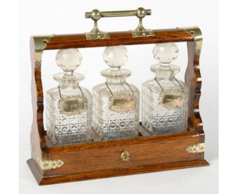 AN EDWARDIAN EPNS MOUNTED OAK TANTALUS WITH THREE CUT GLASS DECANTERS AND STOPPERS AND SET OF THREE LATER SILVER DECANTER LAB