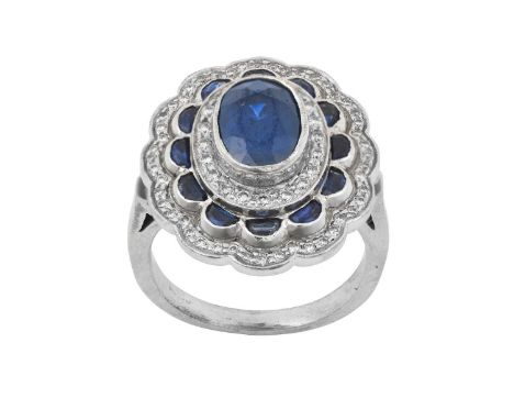 A Sapphire and Diamond Cluster Ringthe oval cut sapphire within a triple stepped border of round brilliant cut diamonds and d