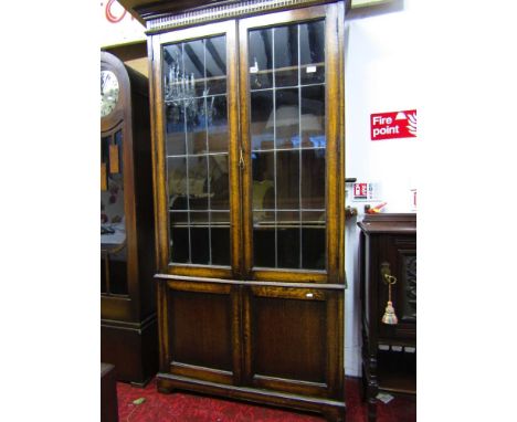 An Edwardian oak bookcase of full height enclosed by four doors, two with leaded light panels beneath a carved frieze