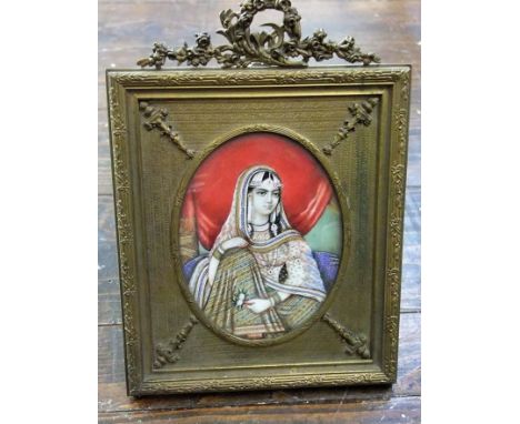 An early 20th century Indian moghul type miniature portrait of oval form of a seated female character in a curtained interior
