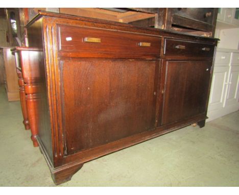 An oak side cupboard of simple form enclosed by two doors and two drawers on short bracket supports.
