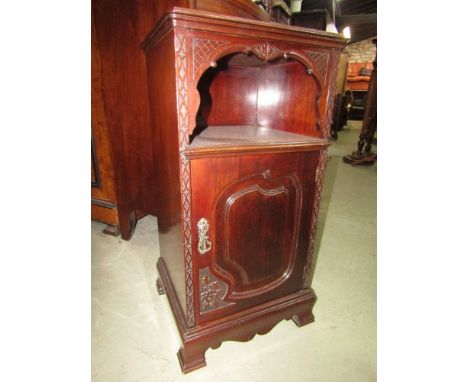 An Edwardian mahogany bedside or lamp table, the lower section enclosed by a carved and panelled door and with open alcove wi