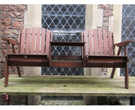 A contemporary teak two seat garden bench with slatted seat and back joined by a central table/platform with parasol hole.